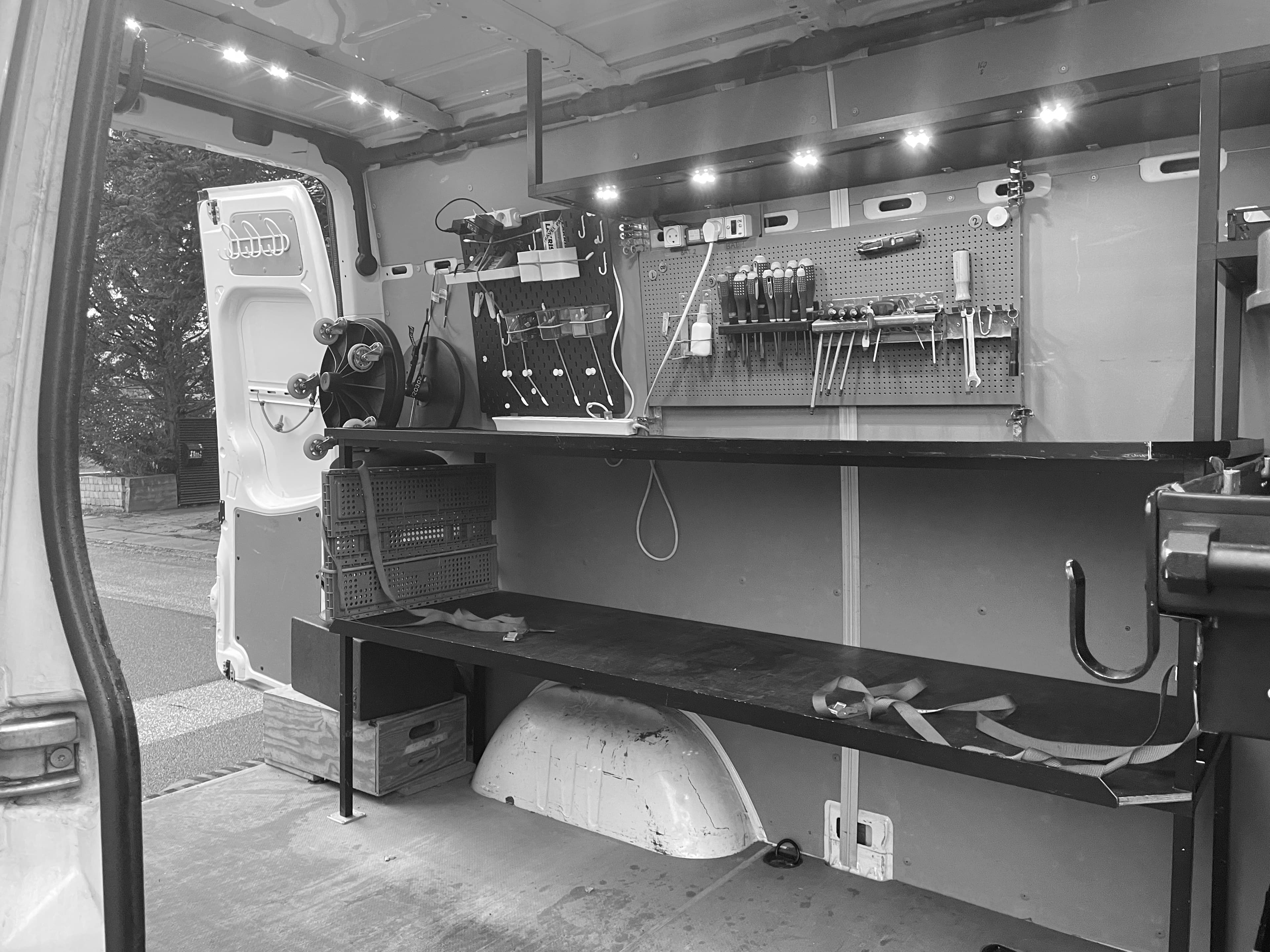 Organized mobile workshop inside a van with a workbench, tool pegboard, and overhead lighting.