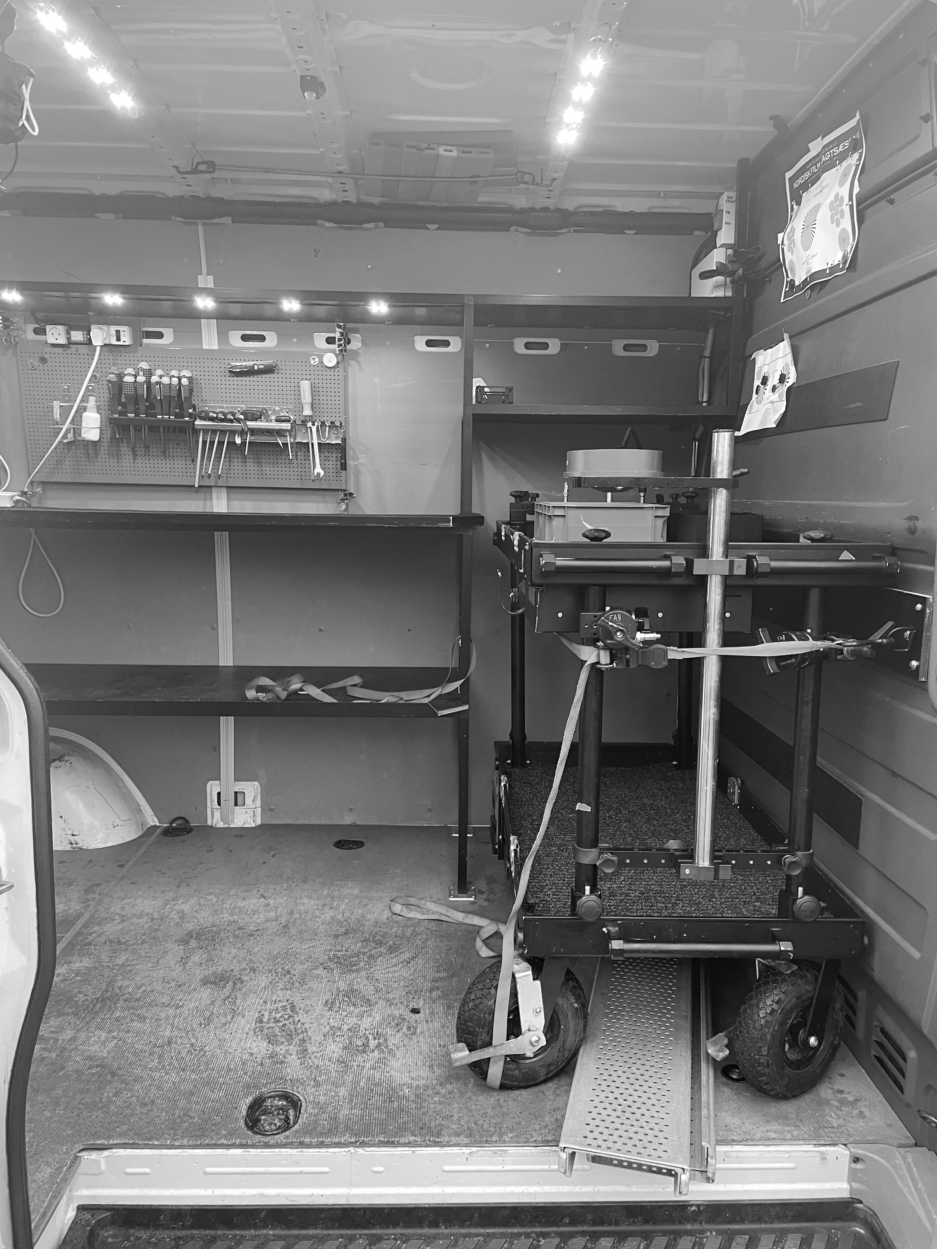 Organized mobile workshop interior with a tool pegboard, shelving, and a secured equipment cart.