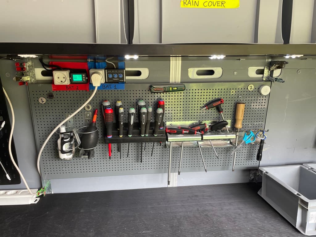 Organized workbench featuring tools on a pegboard, electrical outlets, and overhead storage bins.