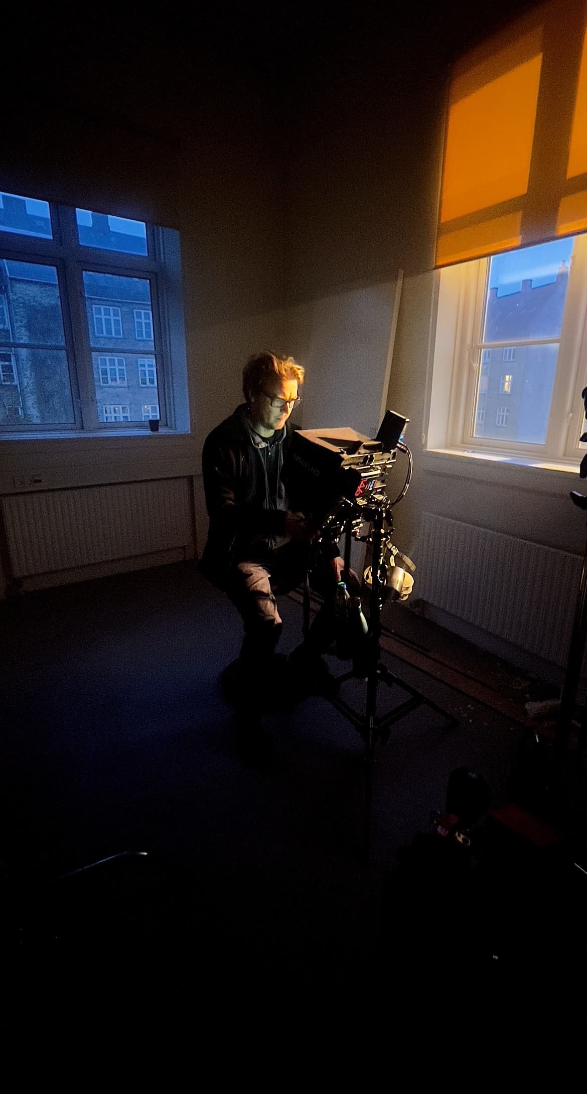 Cinematographer operating a professional camera in a dimly lit room, highlighted by warm orange light.